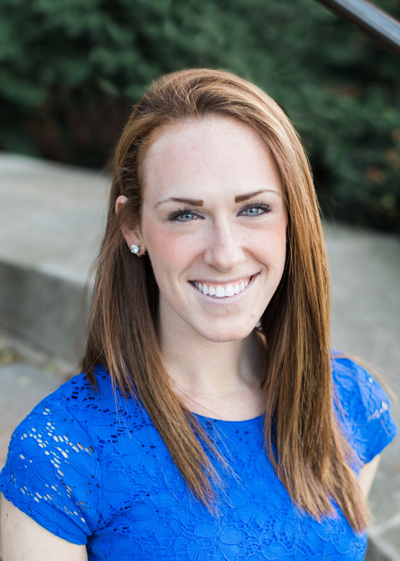 photo of webinar host. A photo of a woman with long reddish hair wearing a blue tshirt.