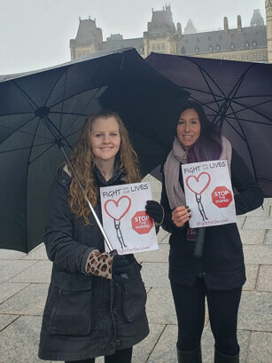photo of two women standing outside under umbrellas holding signs that say "fight for our lives'