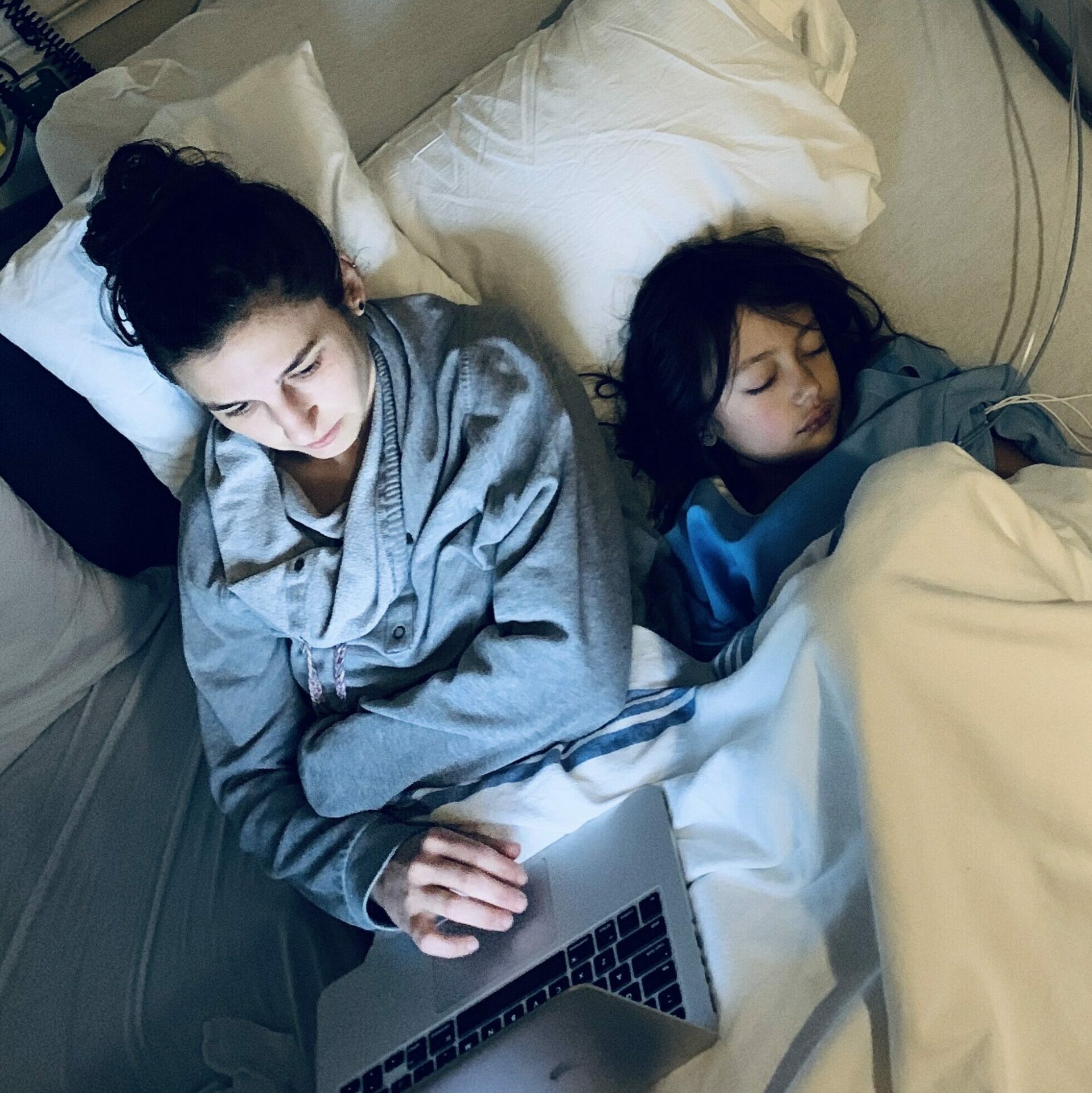 parent writing a blog post on a computer next to a sleeping PFIC patient in a hospital bed